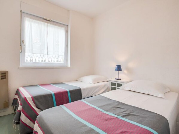 Een slaapkamer met twee bedden, een raam met gordijnen, een nachtkastje met een lamp en een radiator.