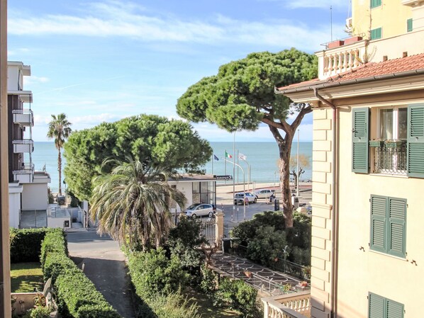 A coastal residential area with a view of the sea, a tree-lined street, and a building with green shutters.