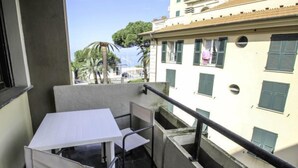 A balcony with a white table and chairs, a concrete floor, and a view of a building with green shutters and a balcony railing. - Caterina by Interhome (Sestri Levante)
