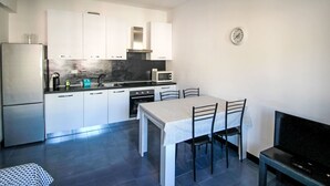 A compact kitchen with white cabinets, a microwave, a stove, and a dining table with chairs. - Caterina by Interhome (Sestri Levante)