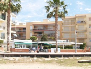 A beachfront restaurant with outdoor seating, palm trees, and a building with balconies in the background. - Horta del Mar by Interhome (Cambrils)