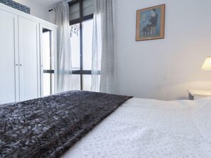 Quarto com cama, janela com cortinas, quadro na parede e mesa de cabeceira com abajur.