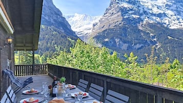 Une table à manger installée à l’extérieur, avec vue sur les montagnes, une terrasse en bois et les montagnes en toile de fond.