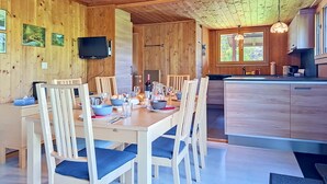 A wooden interior with a dining table set for four, a kitchen with wooden cabinets, and a television mounted on the wall. - Egg-Isch by Interhome (Grindelwald)