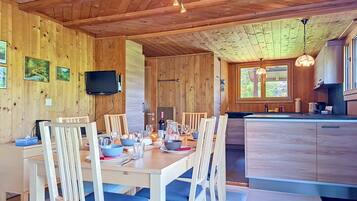 Un intérieur en bois comprenant une table à manger pour quatre personnes, une cuisine avec des meubles en bois et un téléviseur fixé au mur.