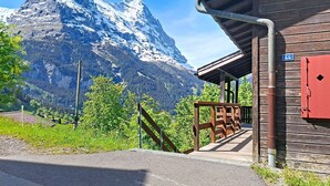 A wooden building with a red door, a staircase leading to a covered area, and a mountain in the background. - Egg-Isch by Interhome (Grindelwald)