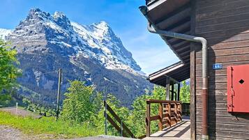 Un bâtiment en bois avec une porte rouge, un escalier menant à une zone abritée et une montagne en arrière-plan.