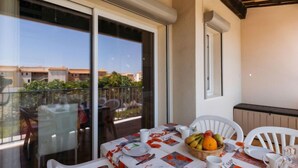A balcony with a table set for dining, featuring a fruit basket and white chairs. - Les Maldives by Interhome (Cap d'Agde)