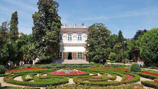 A formal garden with symmetrical flower beds and a classical building with arched windows.