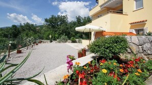 A yellow building with a balcony, a gravel driveway, and a flower garden.