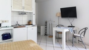 Una cocina compacta con armarios blancos, horno integrado, lavamanos y comedor con mesa y sillas.