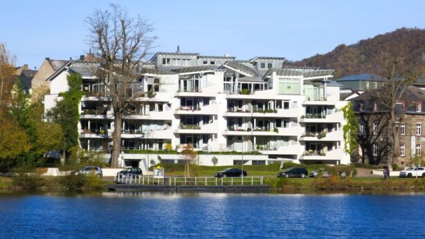 Un edificio residencial de varios pisos con balcones, cerca de una masa de agua.
