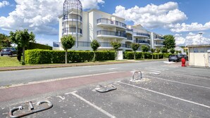 Ein mehrgeschossiges Wohngebäude mit Balkonen, einem Parkplatz und blauem Himmel.