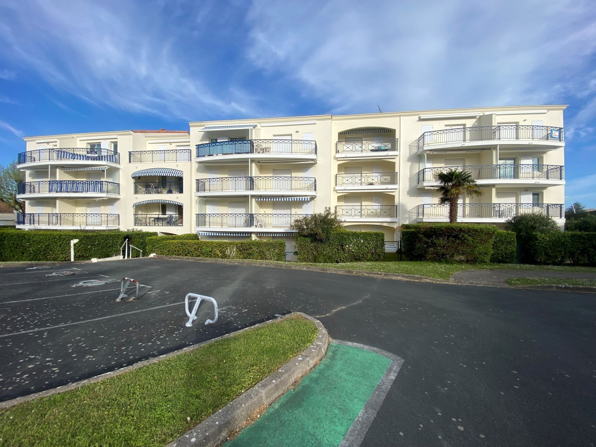 A multi-story residential building with balconies, a parking lot, and a green space.