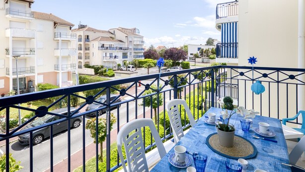 Ein Balkon mit Esstisch, der auf eine Straße mit parkenden Autos und Gebäuden blickt.