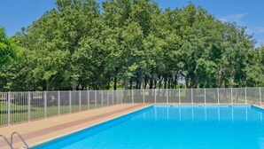 Ein rechteckiger Swimmingpool, umgeben von einem weißen Zaun, vor einer Kulisse aus dichtem Grünwerk.