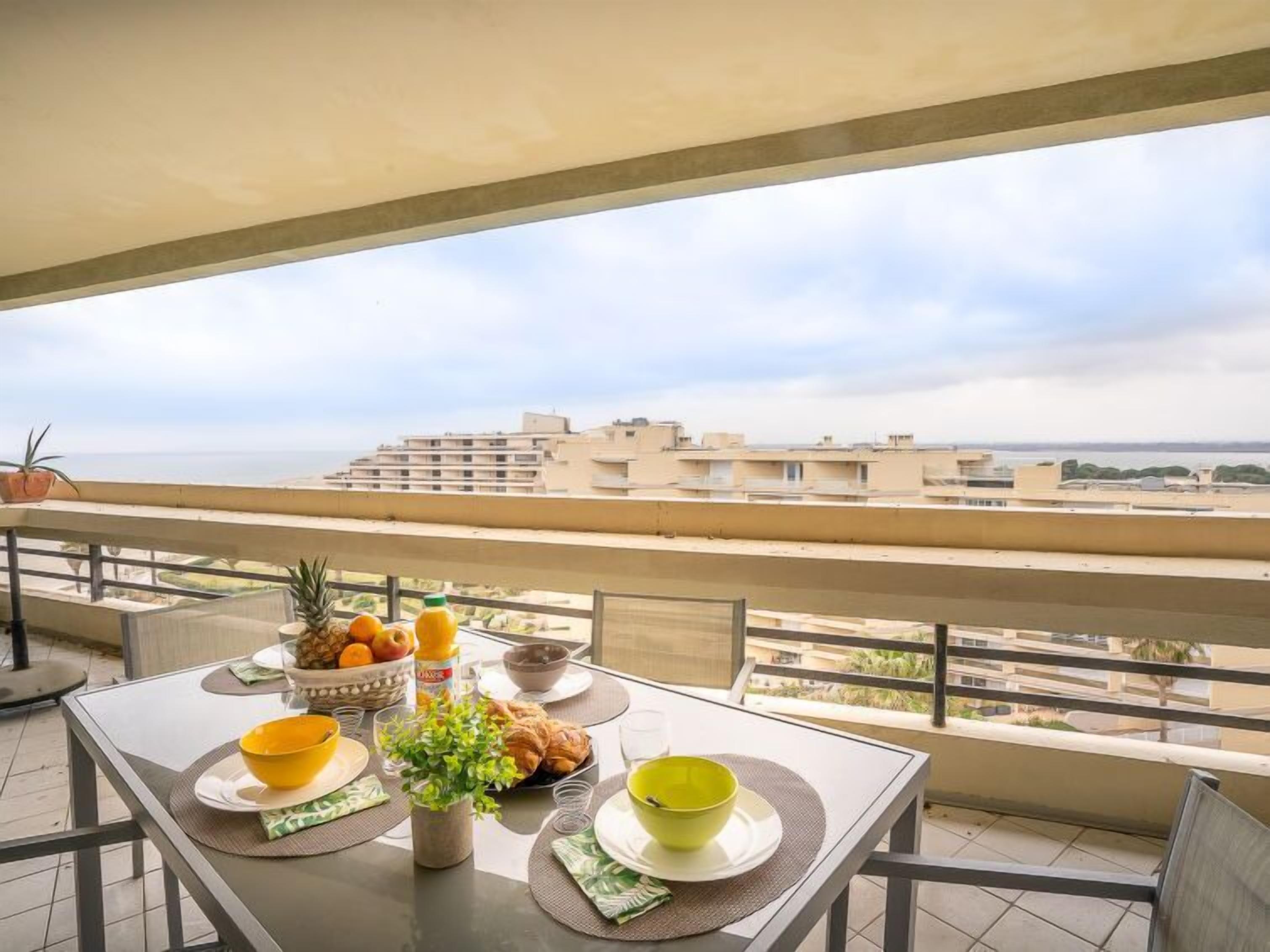 A balcony with a table set for breakfast, overlooking a cityscape.