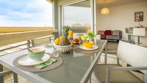 Un balcon avec une table à manger dressée pour le petit-déjeuner, comprenant des fruits et des boissons, donnant sur un paysage urbain.