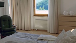 Ein Hotelzimmer mit Bett, Sessel, Kommode und einem Fenster mit Vorhängen.