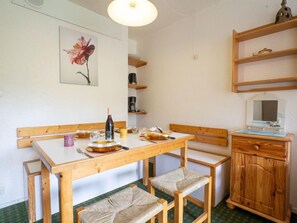 A small, cozy kitchen with a wooden table, two chairs, a wine bottle, and a coffee maker. - Pegase Phenix by Interhome (Le Corbier)