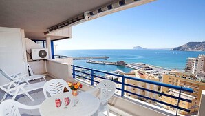 A balcony with white plastic chairs and a table, overlooking a coastal city with buildings and a harbor. - Turquesa Beach 03 by Interhome (Calpe/Calp)