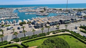 A marina with numerous boats docked, a parking area, and a road with palm trees.