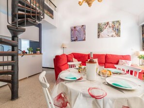 A dining area with a red sofa, a dining table set with plates and cutlery, and a staircase with a black railing.