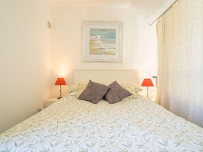 A neatly made bed with a leaf-patterned bedspread, two bedside lamps, and a framed picture on the wall.