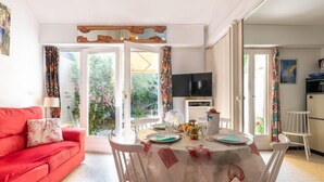 A cozy living room with a red sofa, a dining table set for four, and a TV in the background.