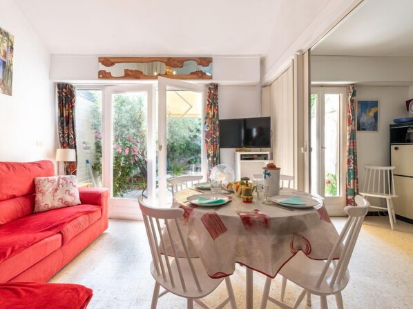 A cozy living room with a red sofa, a dining table set for four, and a TV in the background.