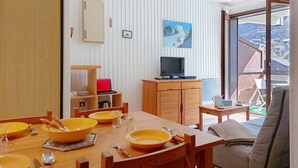 Zona pranzo con tavolo in legno apparecchiato per quattro persone, televisore su un mobile in legno e vista su un paesaggio montuoso attraverso un'ampia finestra.