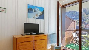 Una stanza con un armadio in legno, una televisione, un tavolo con teiera e tazze, e un'ampia finestra vista su un paesaggio montuoso.