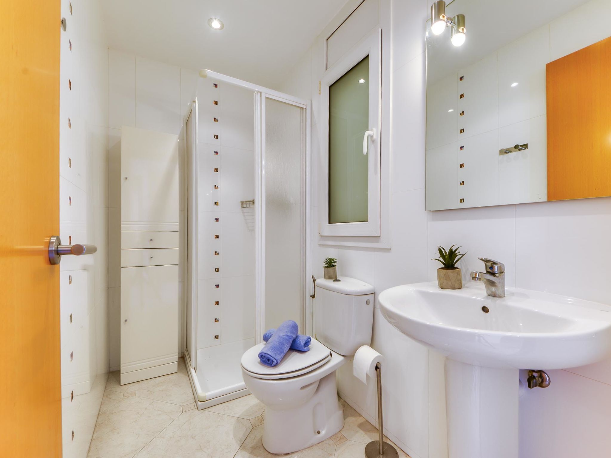A bathroom with a toilet, shower, sink, and a mirror.