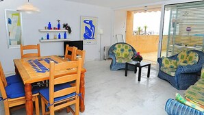 Un coin repas avec une table et des chaises en bois, une petite table d’appoint avec un vase, et une chaise agrémentée d’un coussin coloré.