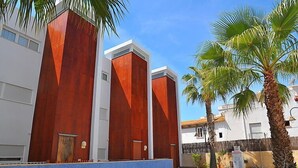 Une piscine à l’intérieur bleu, entourée d’un bâtiment blanc orné d’éléments verticaux rouges et de palmiers.