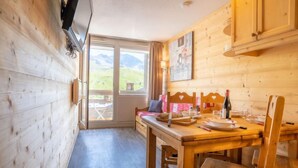 Uma cabana de madeira com uma mesa de jantar, cadeiras e uma televisão fixada na parede.