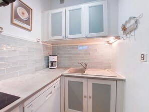 A compact kitchen with white cabinets, a coffee maker, and a sink.