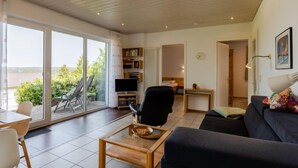 Ein großzügiger Wohnbereich mit einer großen Schiebeglastür, die zu einer Außenpatio führt, einem bequemen Sofa, einem Holztisch und einem Fernseher auf einem Standfuß.