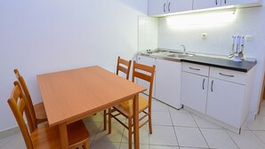 Een kleine keuken met witte kastjes, een houten eettafel en een inbouwfornuis.