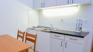 Een kleine keuken met witte kastjes, een zwart aanrecht en een houten eettafel met stoelen.