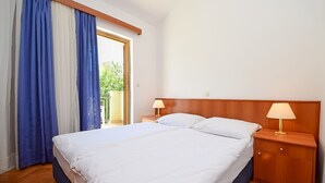 Hotelkamer met een bed, twee nachtkastjes met lampen, een houten hoofdeinde en uitzicht door een deur naar een buitenruimte.