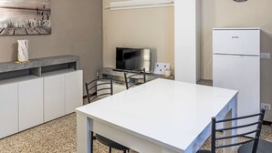 Una cucina funzionale con un tavolo bianco, un frigorifero, un televisore e un quadro appeso al muro.