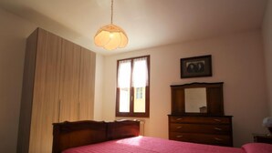 Una camera da letto con un letto, una cassettiera, uno specchio e una finestra con tende.