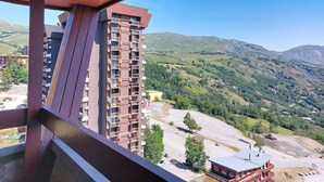 A high-rise building with multiple balconies, a view of a mountainous landscape, and a construction site in the foreground. - Lunik Orion by Interhome (Le Corbier)