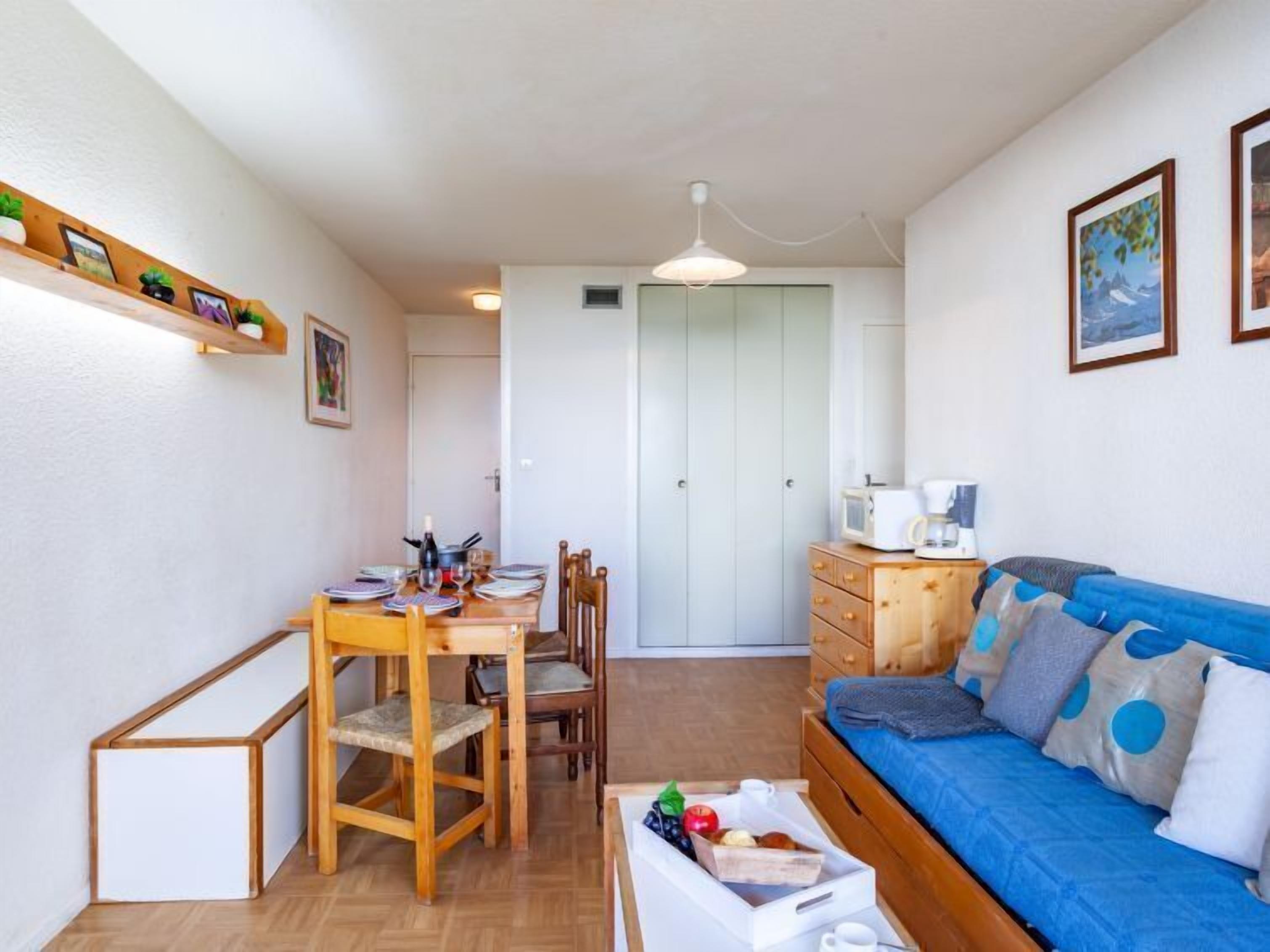 Un espace de vie compact comprenant un coin repas, une kitchenette et un lit agrémenté d’oreillers à pois.
