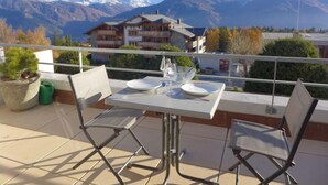 A balcony with a table set for two, overlooking a mountain range. - Jeanne D'Arc Apt. D-33 by Interhome (Crans-Montana)