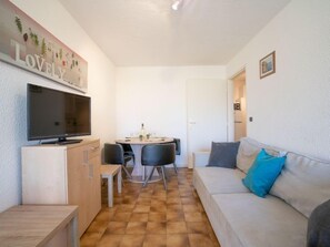 Un espace de vie compact comprenant un téléviseur, une table à manger avec des chaises, un canapé avec des coussins et un meuble de rangement.
