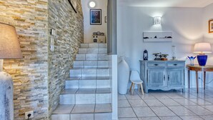 A staircase with a stone wall on one side and a white wall on the other, leading to a landing with a white chair and a blue cabinet. - Eden Parc by Interhome (Lacanau)
