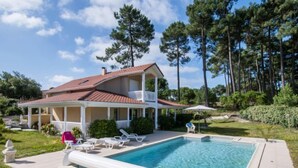 A two-story house with a swimming pool, surrounded by trees and a well-maintained lawn. - Eden Parc by Interhome (Lacanau)
