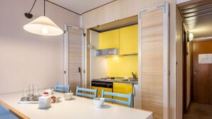 A compact kitchen with yellow cabinets, a white countertop, and a dining area with blue chairs. - Universo by Interhome (Courmayeur)